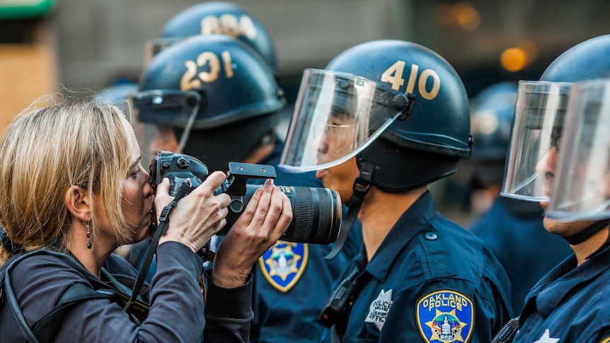 A photographer leans close to a line of police officers at a protest