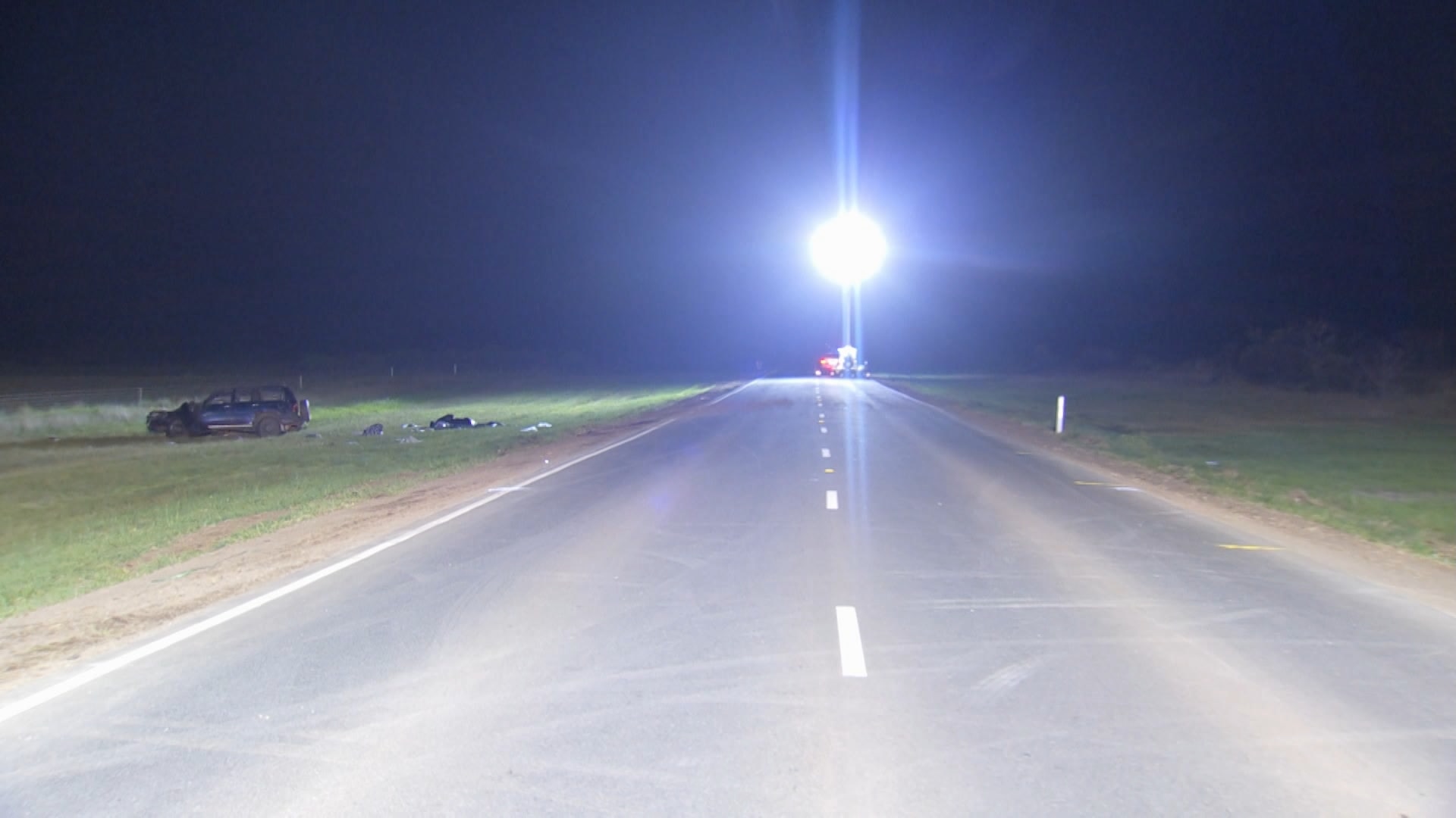 A vacant outer-Melbourne road with a badly damaged car on grass to the left of the road