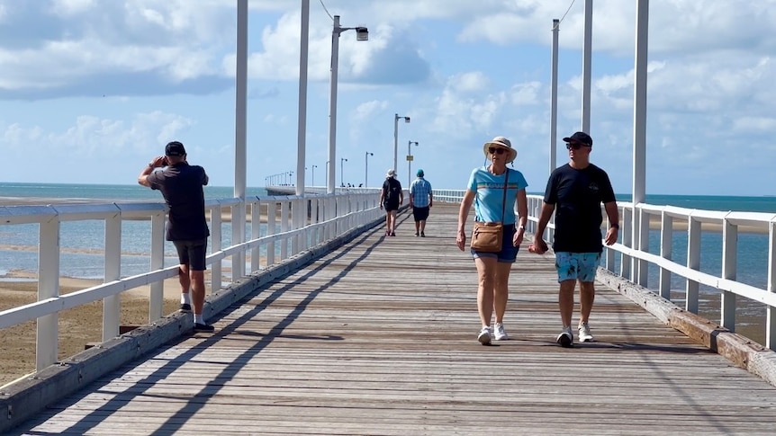 People stroll down a pier on a sunny day at the beach 