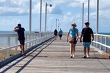 People stroll down a pier on a sunny day at the beach 