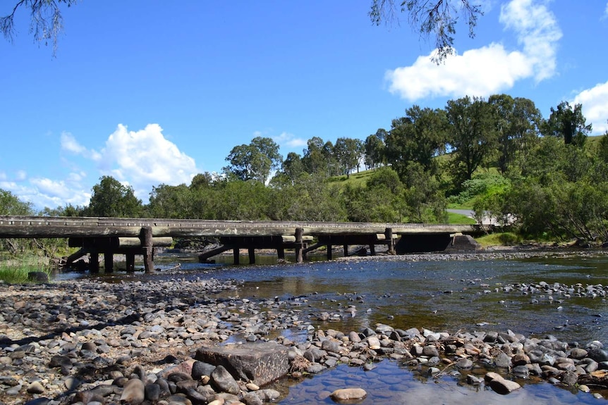 Wooden bridge over wide shallow creek on sunny day blue sky