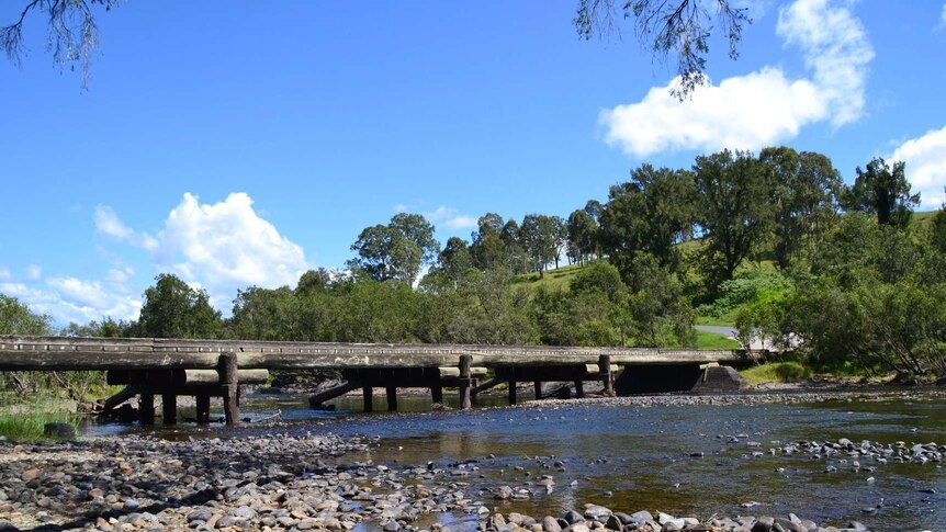 Wooden bridge over wide shallow creek on sunny day blue sky