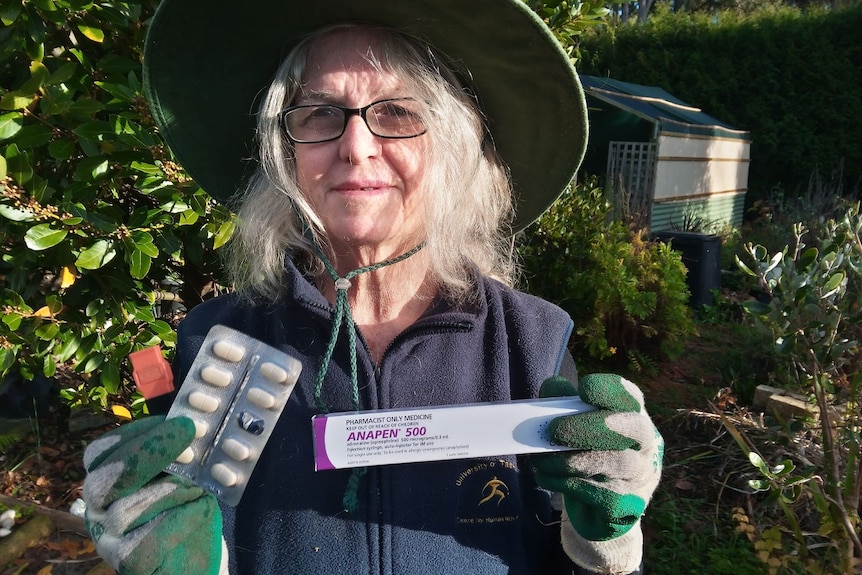 a woman holds an adrenaline pen and anti-inflammatory tablets in a garden