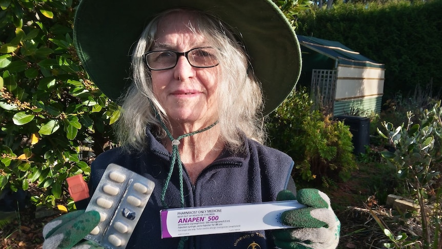 A woman holds an adrenaline pen and anti-inflammatory tablets in a garden.