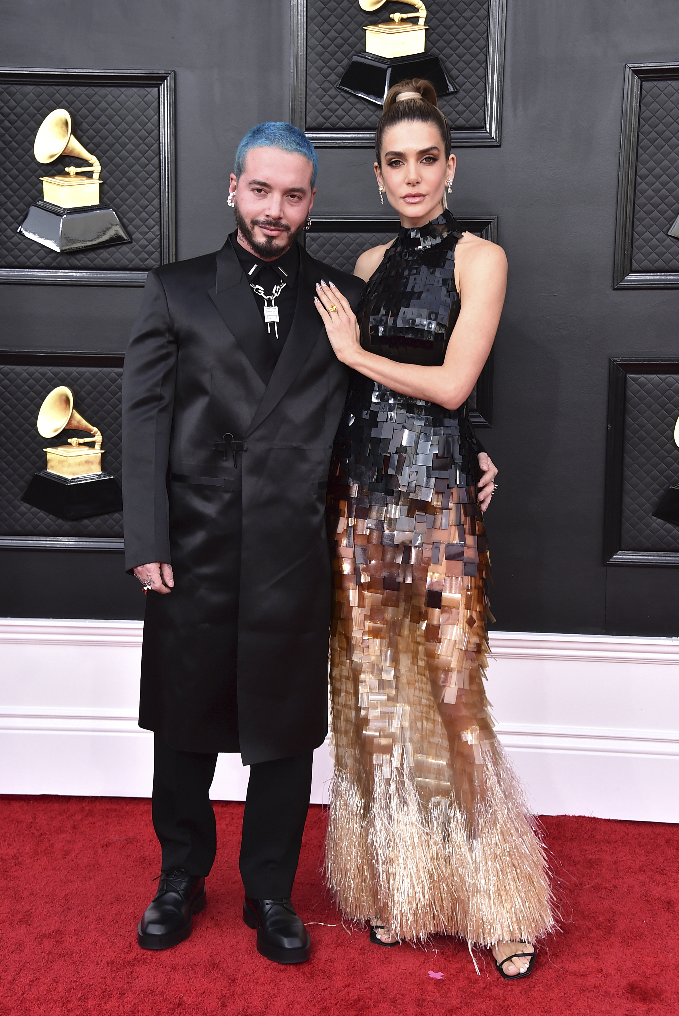 J Balvin and Valentina Ferrer  stand on the red carpet arm in arm. balvin has bright blue short cropped hair