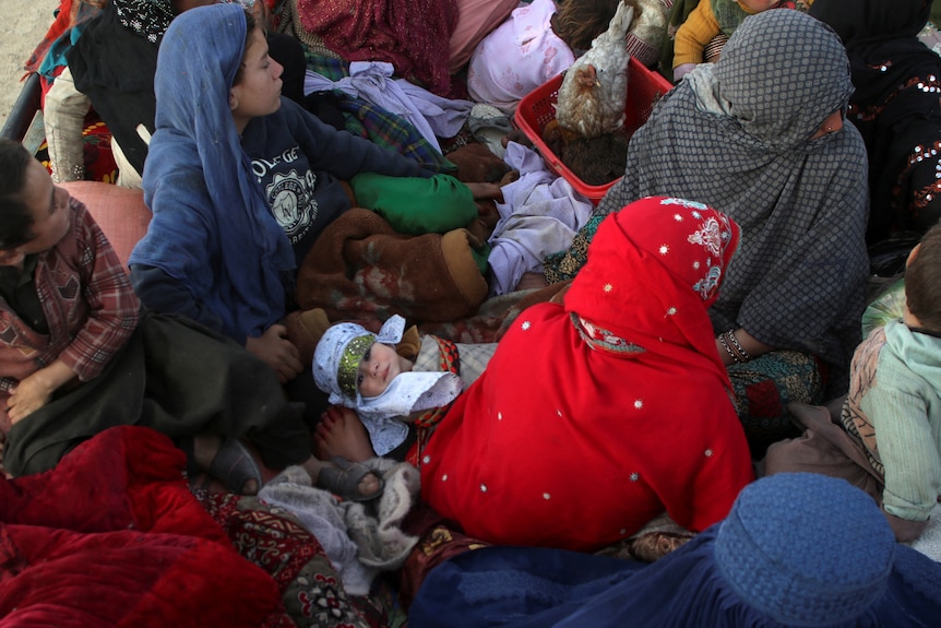 A baby is surrounded by a crowd of people sitting on a floor.