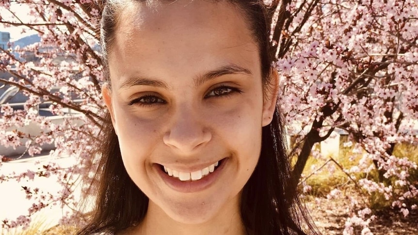 Young woman smiles while standing in front of cherry blossoms