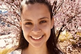 Young woman smiles while standing in front of cherry blossoms