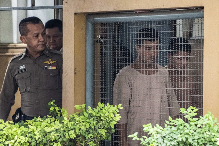 Myanmar migrant workers Zaw Lin and Win Zaw Htu  pictured behind bars, guarded by Thai police