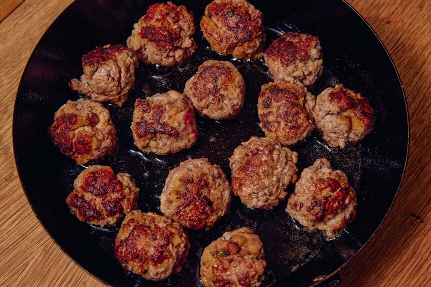 A shallow frying pan with a cluster of small meatballs frying in oil
