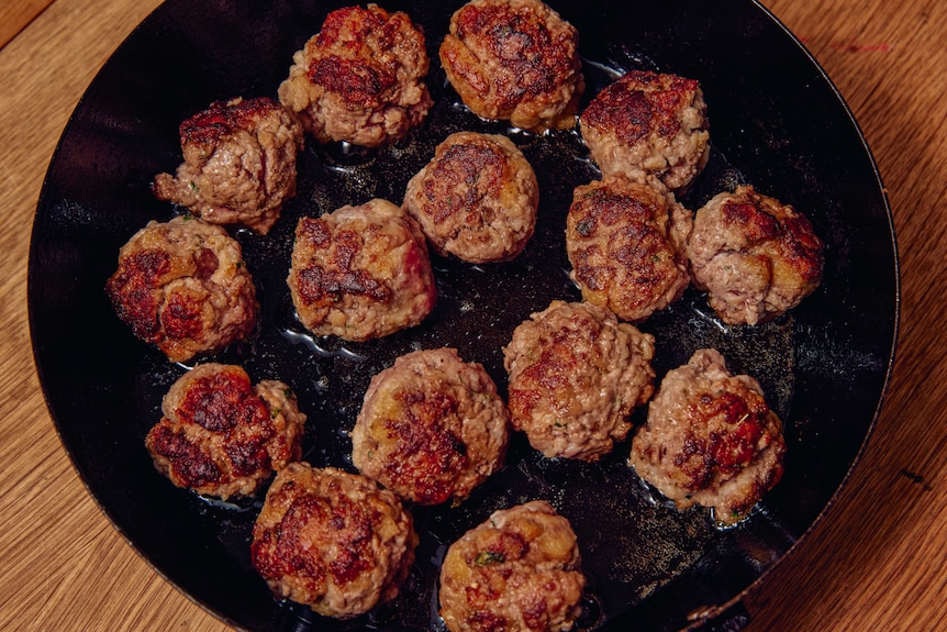 A shallow frying pan with a cluster of small meatballs frying in oil