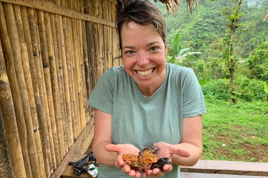 Frog biologist smiling at the camera while holding out a handful of frogs.