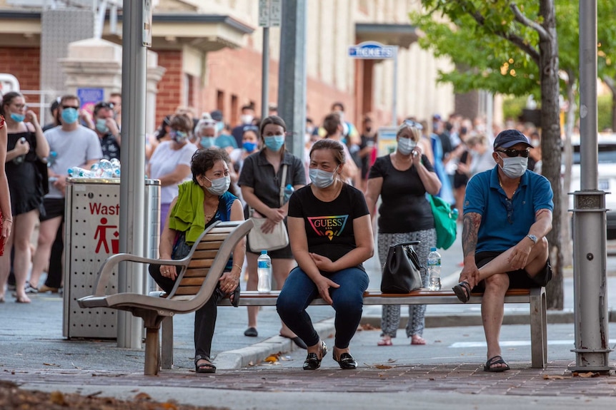 A long line of people wearing face masks stretches down a block.