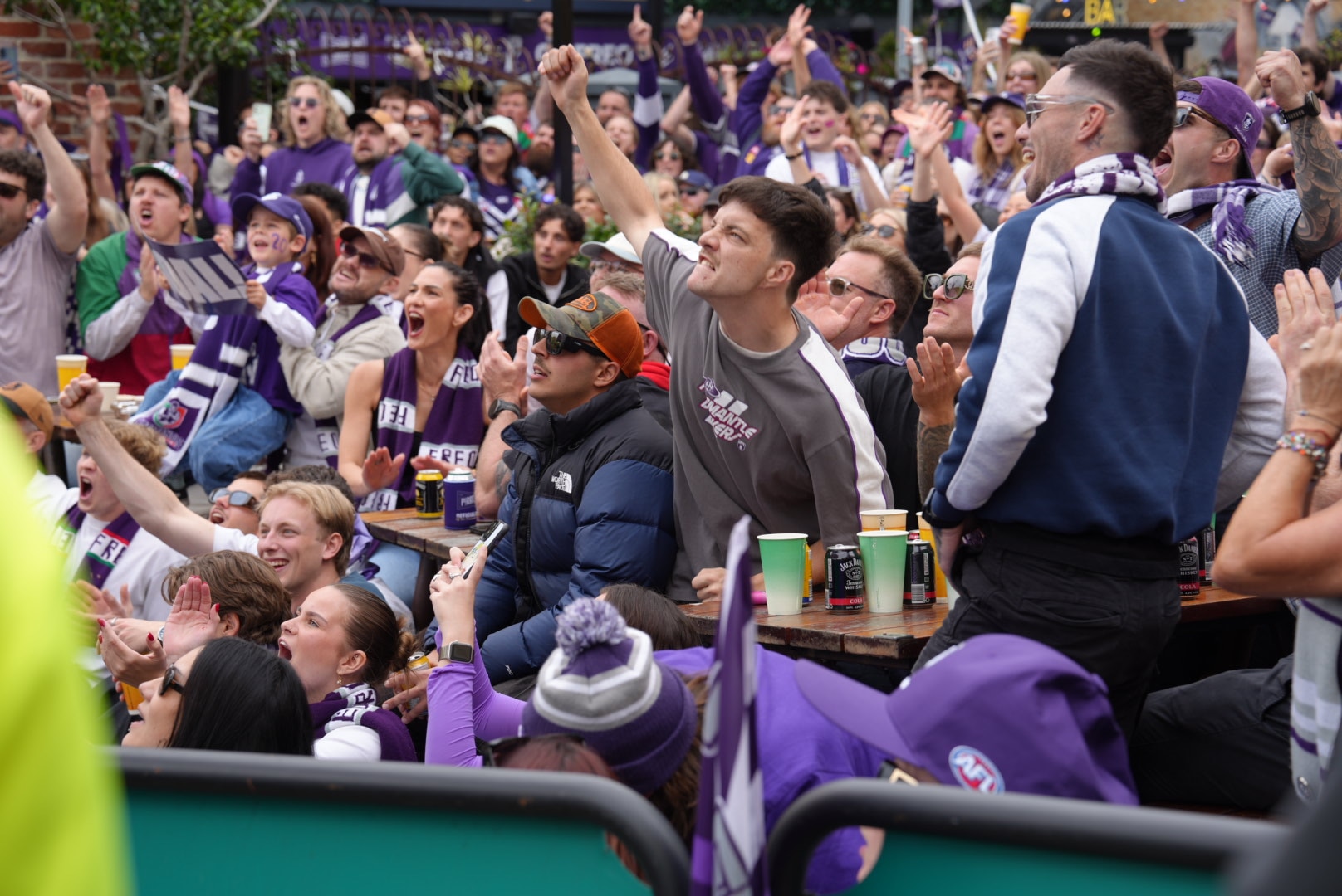 Fremantle Dockers fans wearing purple and white scarves and hats at a street bar