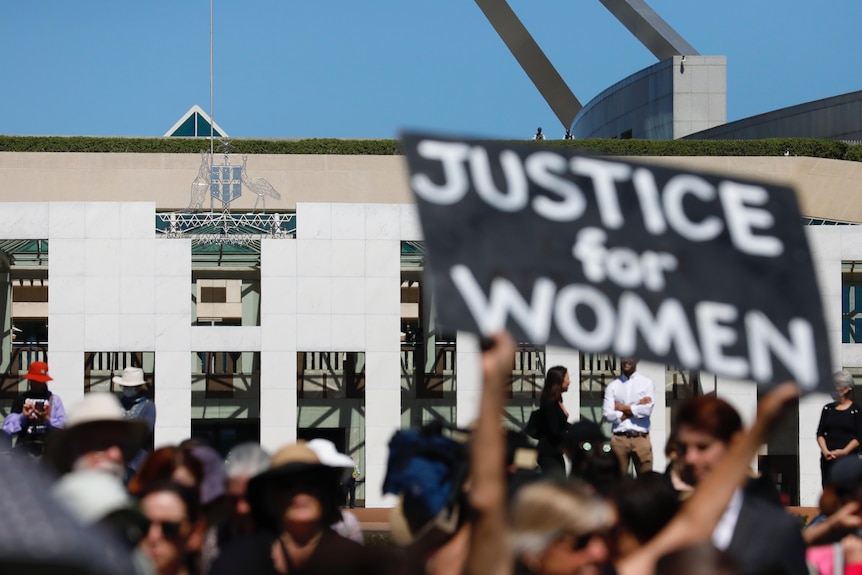A protest sign reading JUSTICE FOR WOMEN stands outside Parliament House in Canberra.