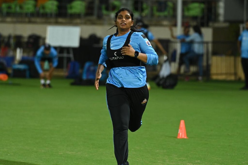 A woman in cricket gear runs on an oval.