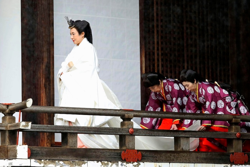 Embress Masako dress in a white robe, two women laying the robe behind her.