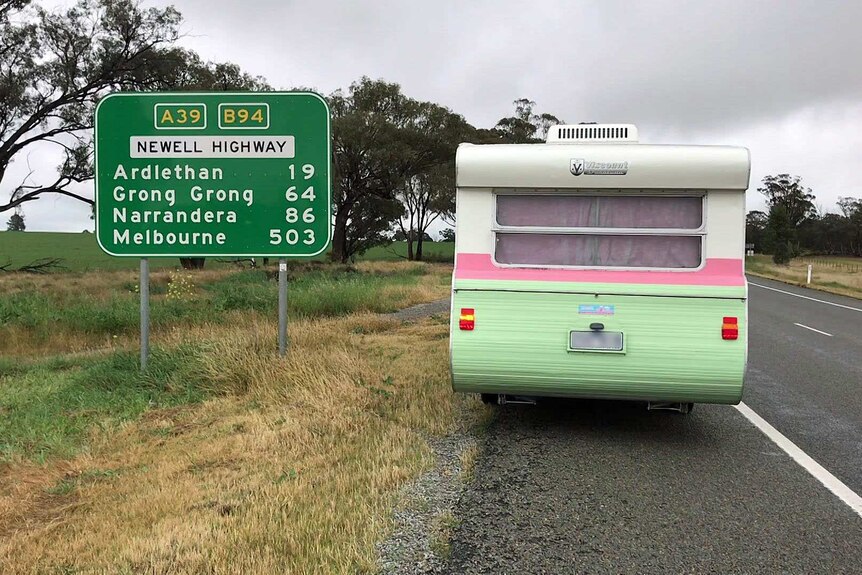 A caravan painted white, pink and green parked on the side of a highway