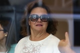 A woman wearing sunglasses photographed through a glass window.