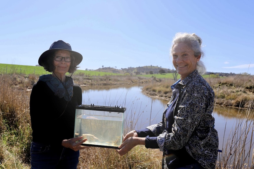 Two smiling woman holding a small glass fish tank