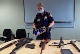 Tasmanian police officer Michelle Combes holds a pistol and displays other weapons found  in a Devonport house.