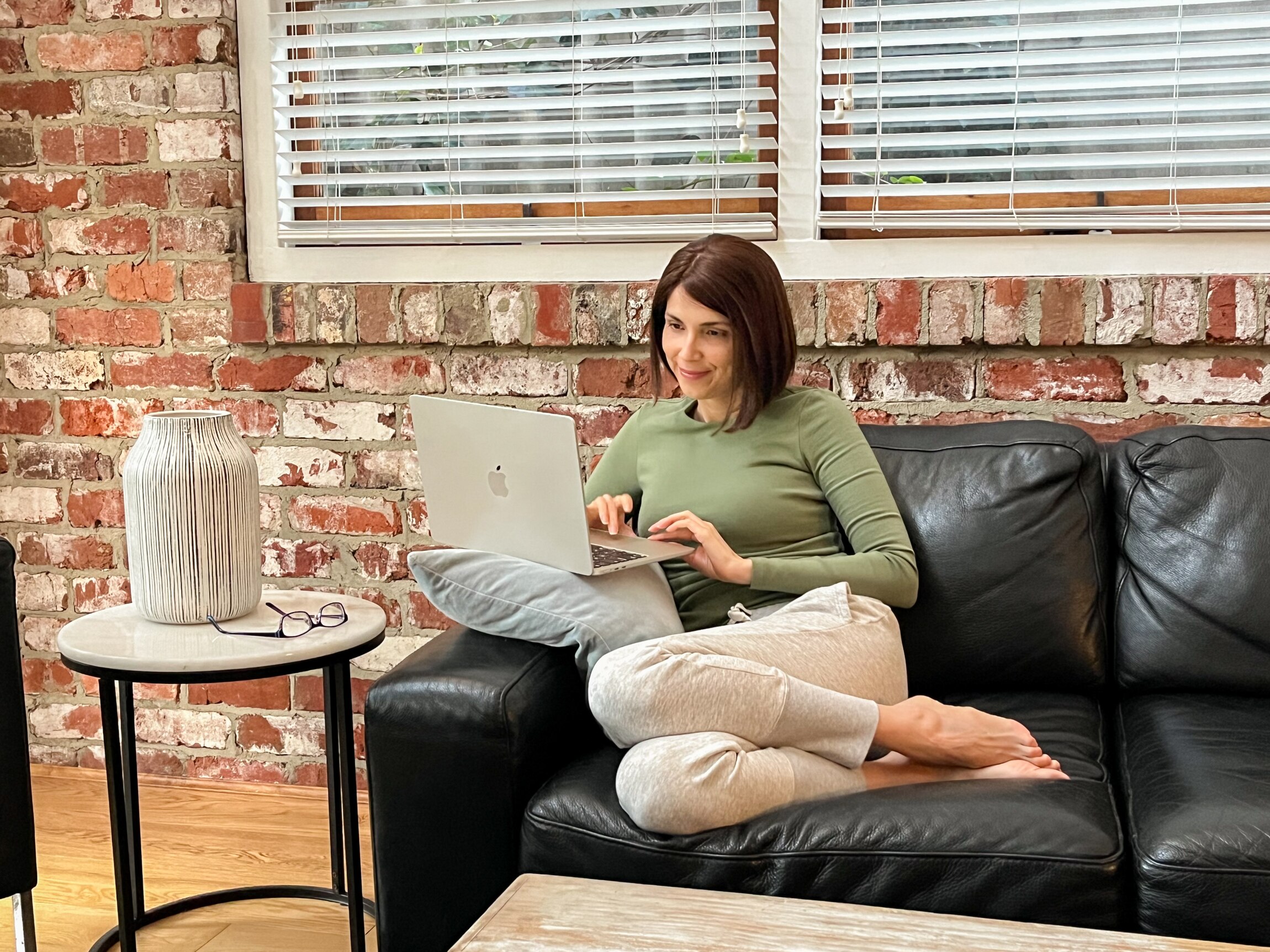 Natalia Hodgins sits on a sofa in comfortable clothes, smiling at her laptop and she communicates with friends online.
