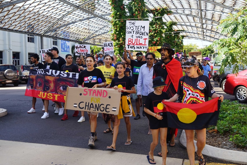 People are holding signs saying 'Black Lives Matter' as they march through Darwin City.