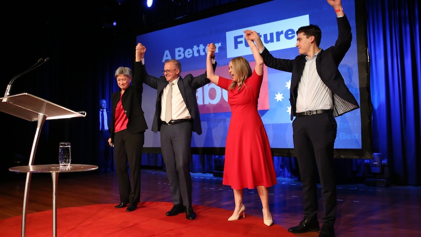 Anthony Albanese on stage with Penny Wong, Jodie Haydon, and Nathan Albanese holding each other hands high