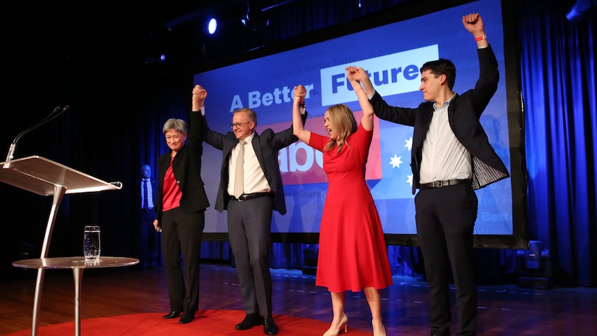 Anthony Albanese holds up hands with Penny Wong, his partner and son on a stage