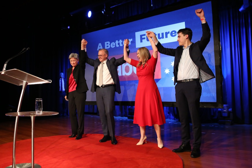 Anthony Albanese holds up hands with Penny Wong, his partner and son on a stage