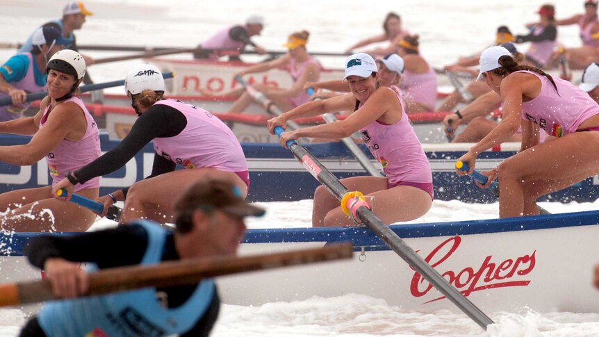 Women surf boat crews power through the surf.