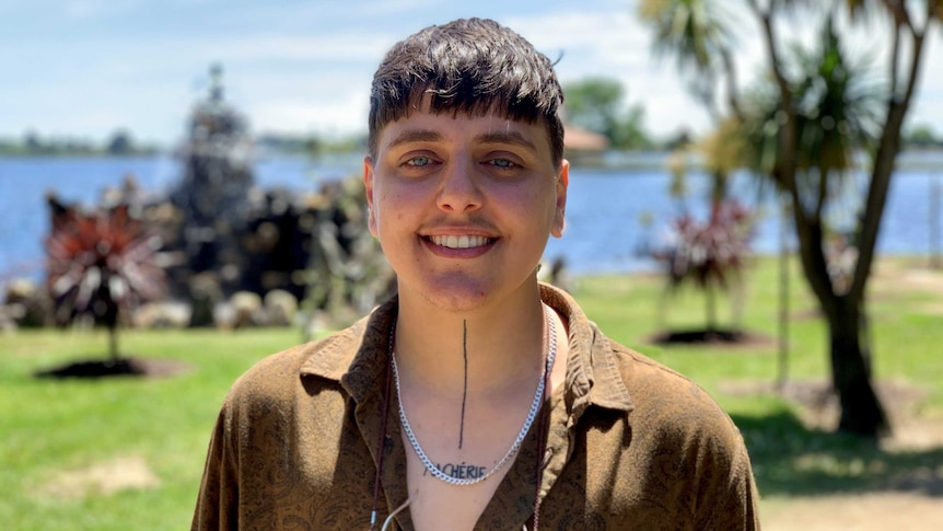 A person smiles at the camera in front of a lake and water feature in Ballarat