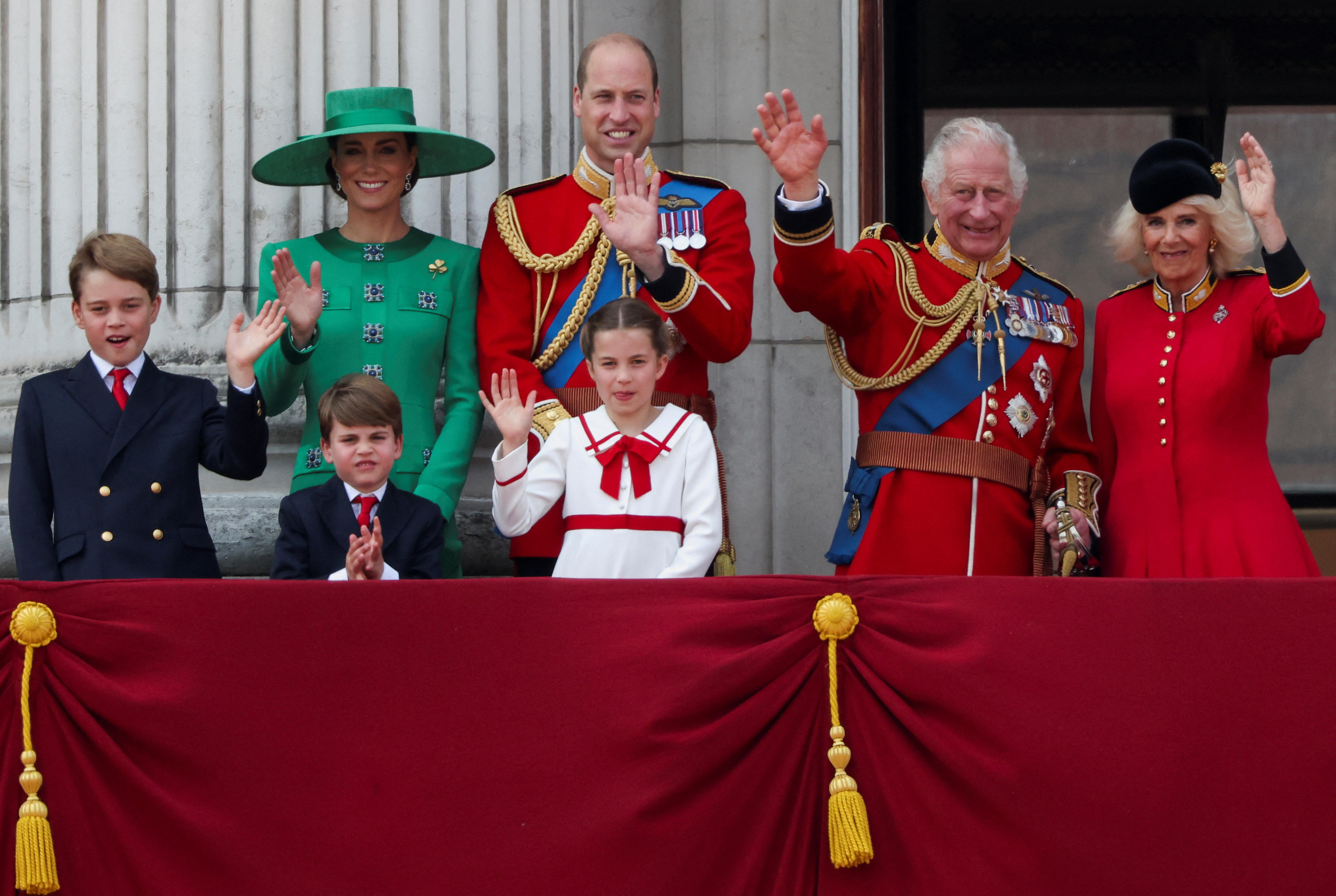 Three children, their mum and dad and their grandparents wave while standing on a balcony.