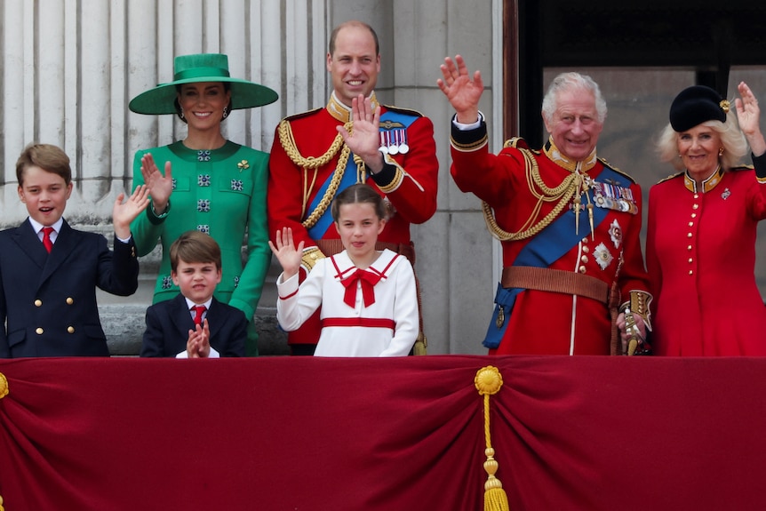 Three children, their mum and dad and their grandparents wave while standing on a balcony.