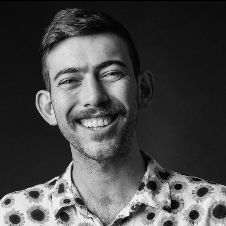 A man in a patterned shirt, with cropped hair and light facial hair, smiles for the camera