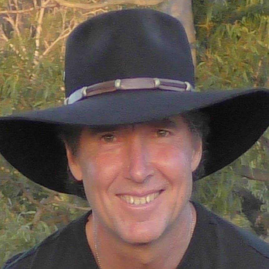 Man in Akubra style hat smiling in bush, wearing black shirt