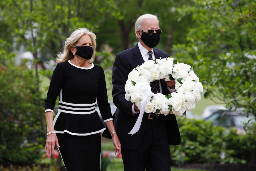 Joe and Jill Biden holding a floral wreath while wearing face masks