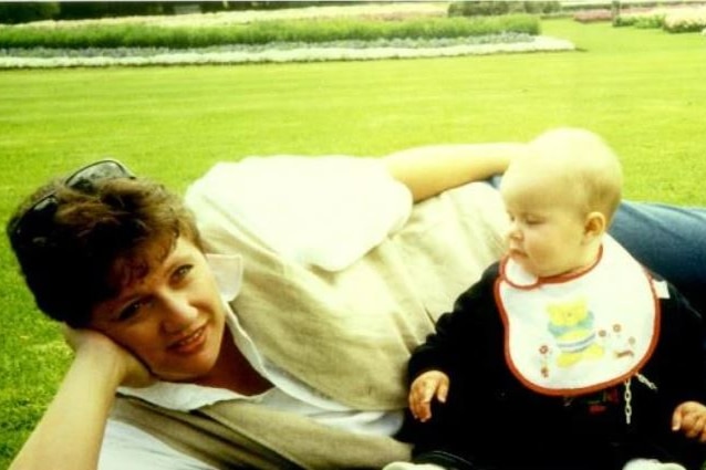 a woman lying on the green grass with a baby by her side