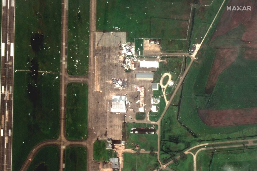 Scattered buildings are seen destroyed and surrounded by debris from a satellite image.