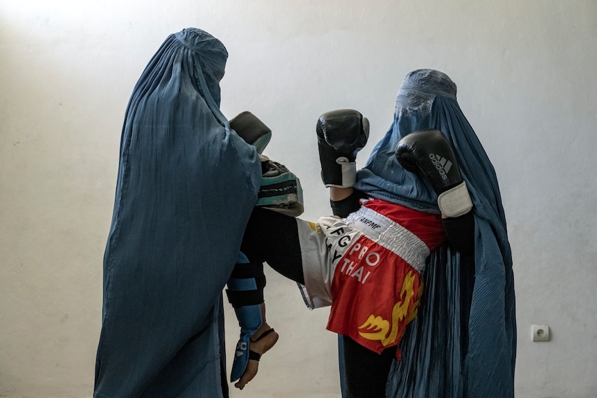 练习拳击的阿富汗妇女穿着罩袍和拳击手套摆姿势拍照。
