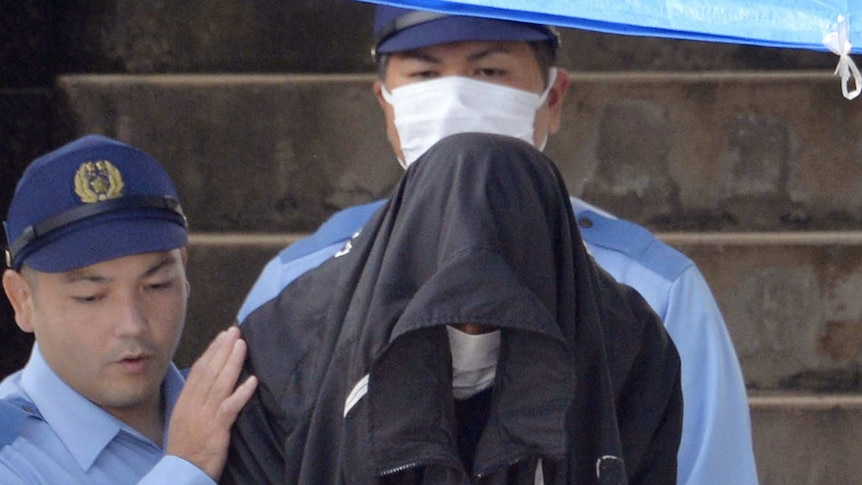 Police lead a man whose face is obscured by a hood.