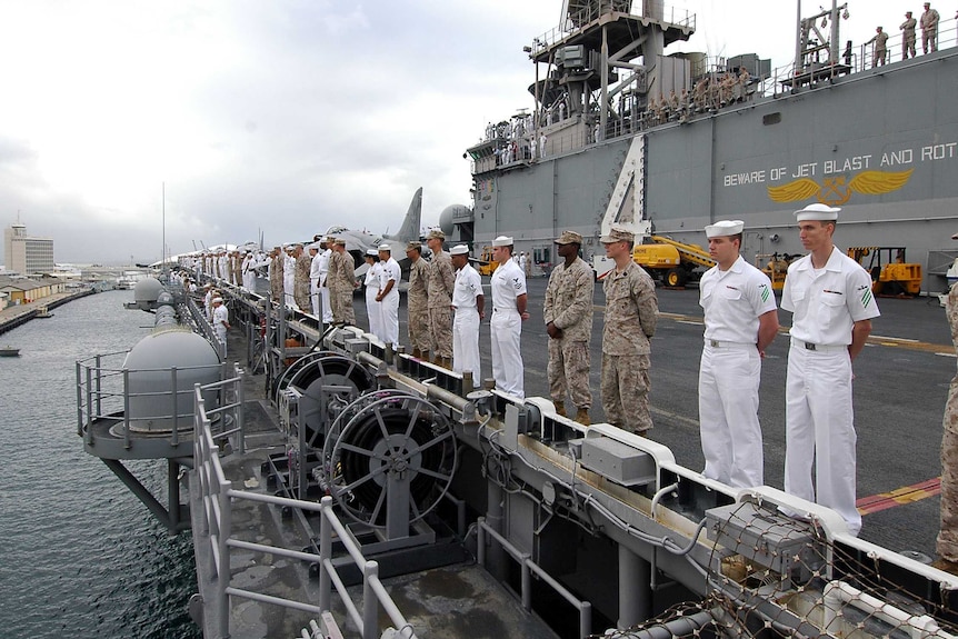 A row of sailors and marines standing on a ship looking out toward water and Fremantle port.