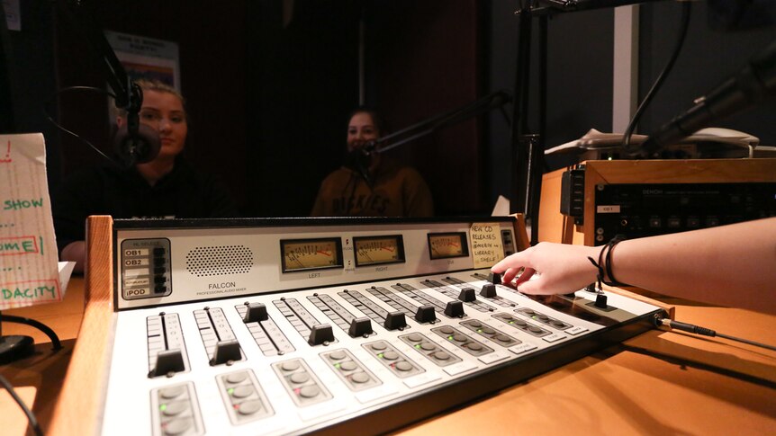 A close up of a radio panel with Jesse and Teegan in the background.