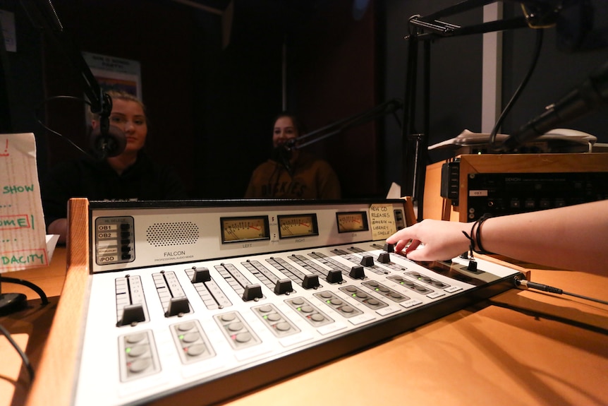 A close up of a radio panel with Jesse and Teegan in the background.
