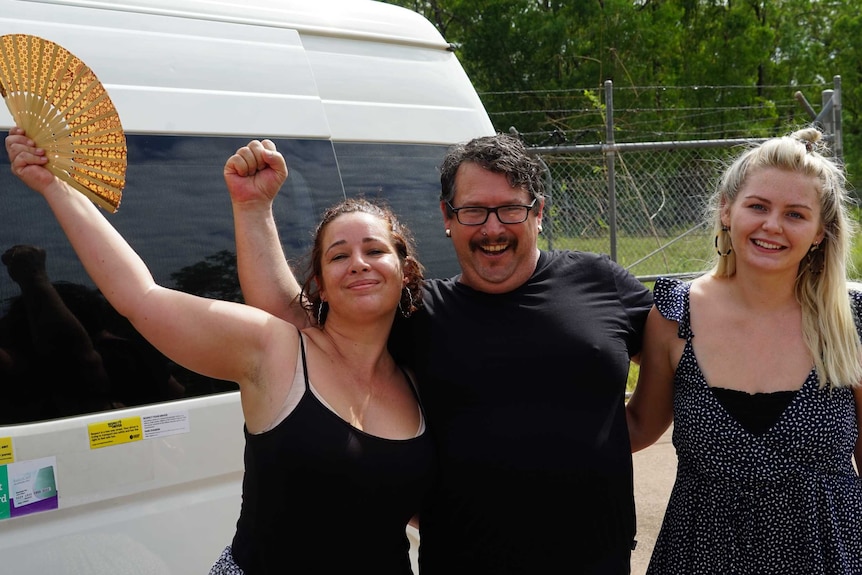 Carla Muir, Joe Edwards, and Ella Worthington have their hands around each other and are smiling to the camera.