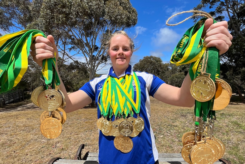 Phoebe Mitchell pictured holding and wearing at least two dozen medals for swimming.