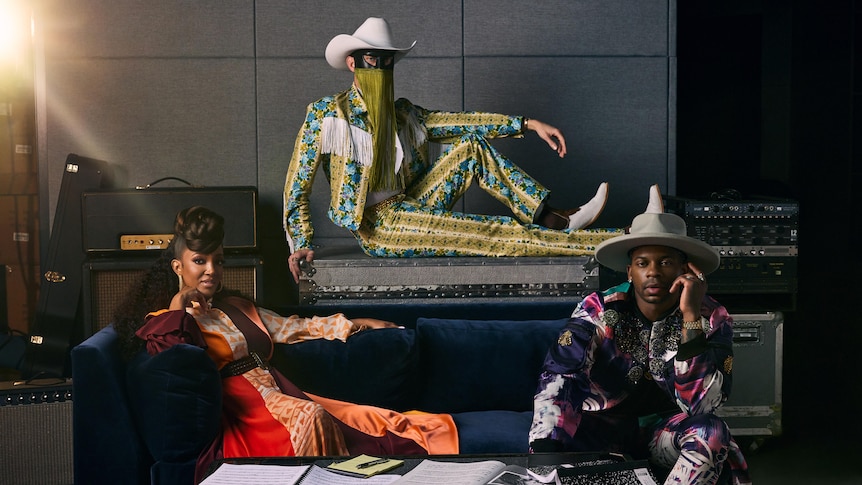 Jimmie Allen, Mickey Guyton and Orville Peck posing in colourful outfits, Orville wearing a face mask