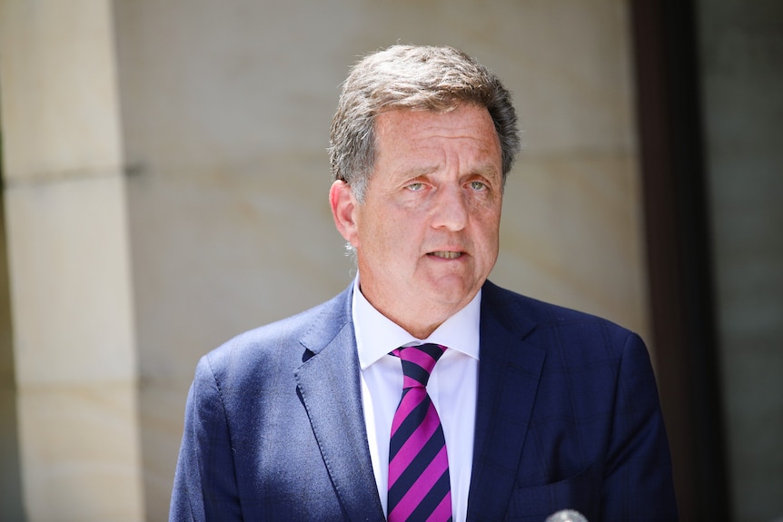 A man in a suit and tie speaks at a press conference. 