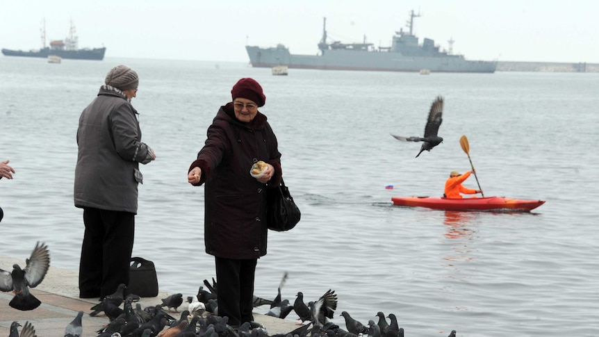 Crimean women feed birds as Russian warships cruise off Sevastopol