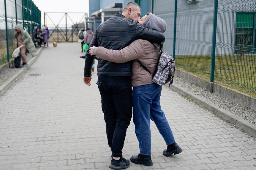 a husband hugs and kisses his wife at the border between Poland and Ukraine